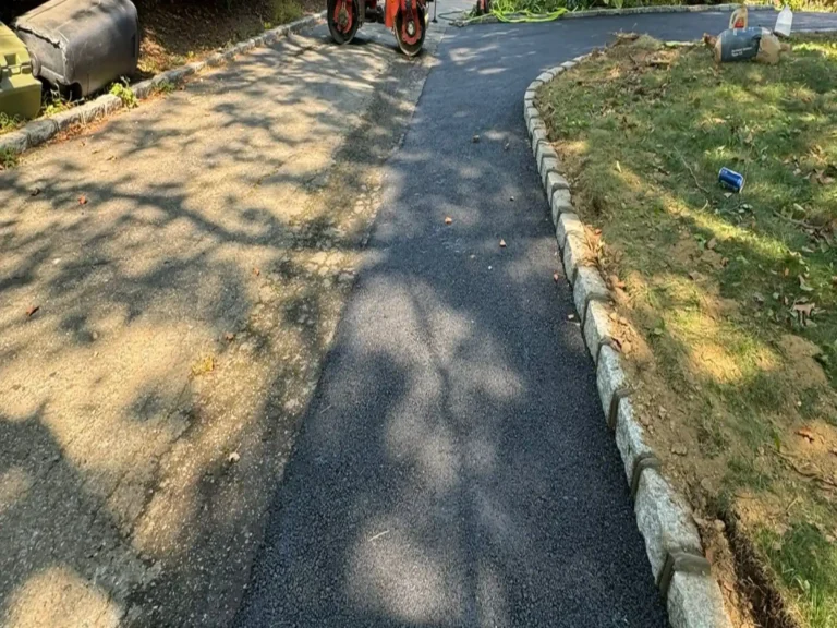 New asphalt driveway with a stone block border along the lawn